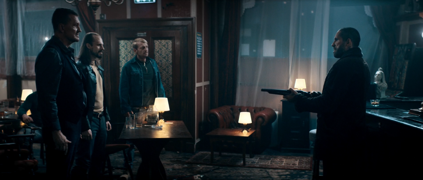 Scott Adkins tenant en joue ses adversaires dans un pub