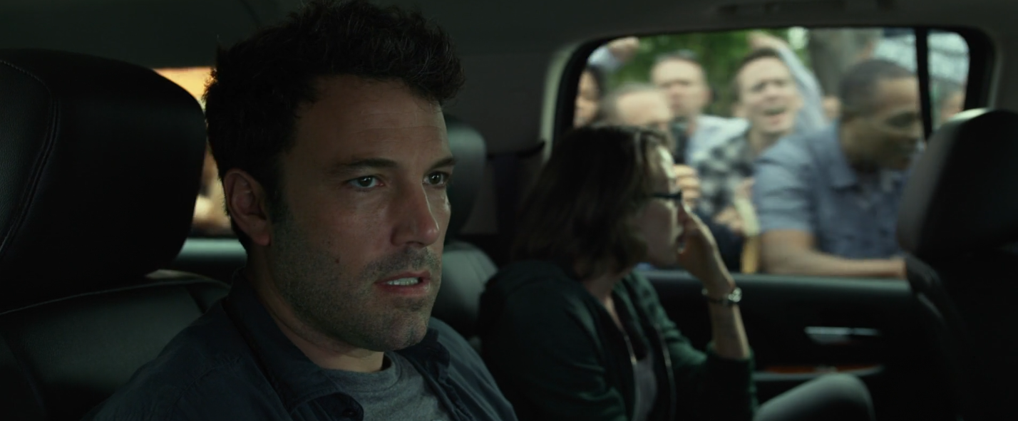 Nick Dunne à l'intérieur d'une voiture entourée par la presse