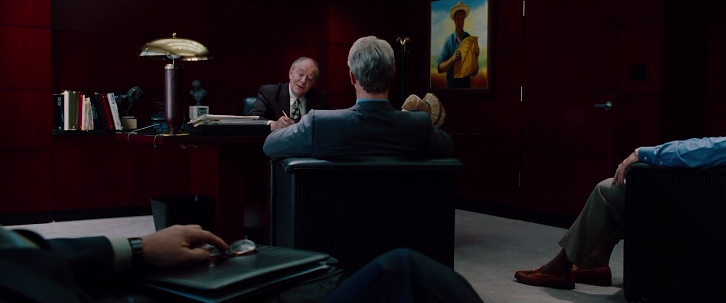 le même plan large sur Wigand mais assis et entouré par des personnes