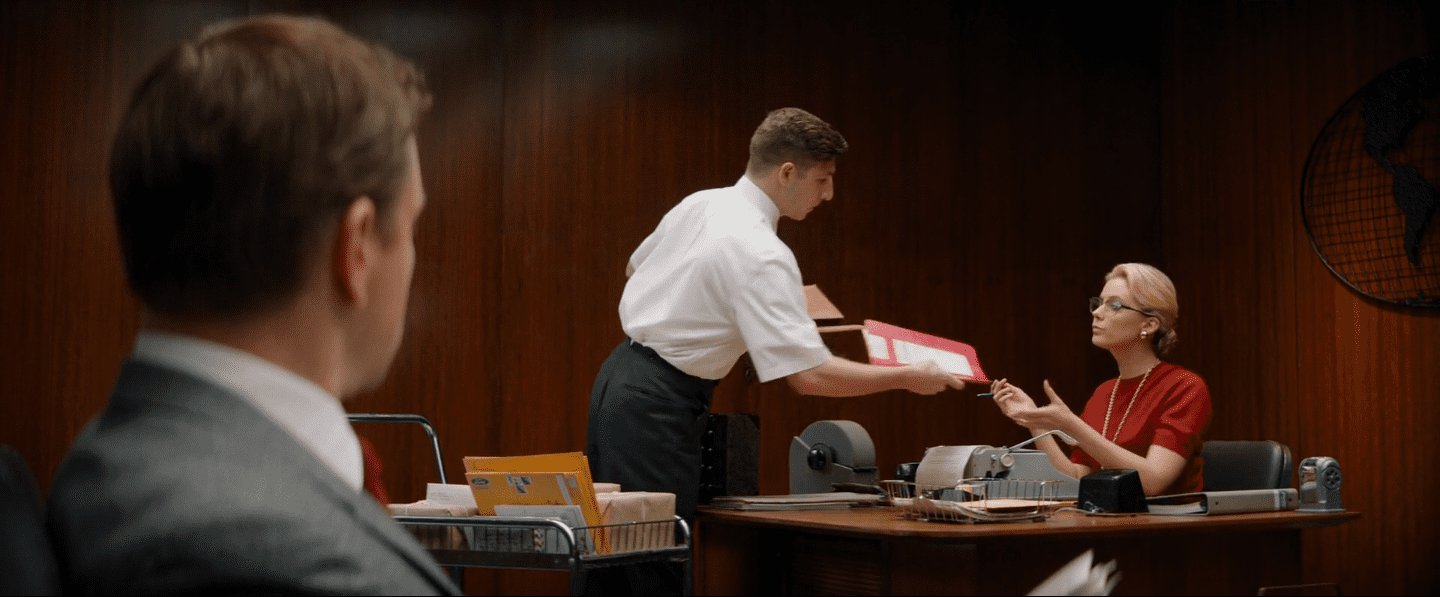 Un assistant entre dans le cadre et donne un dossier à une secrétaire